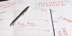 the word 'pay day' written on a notebook surrounded by overdue bills