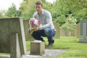 Man placing flowers near headstone