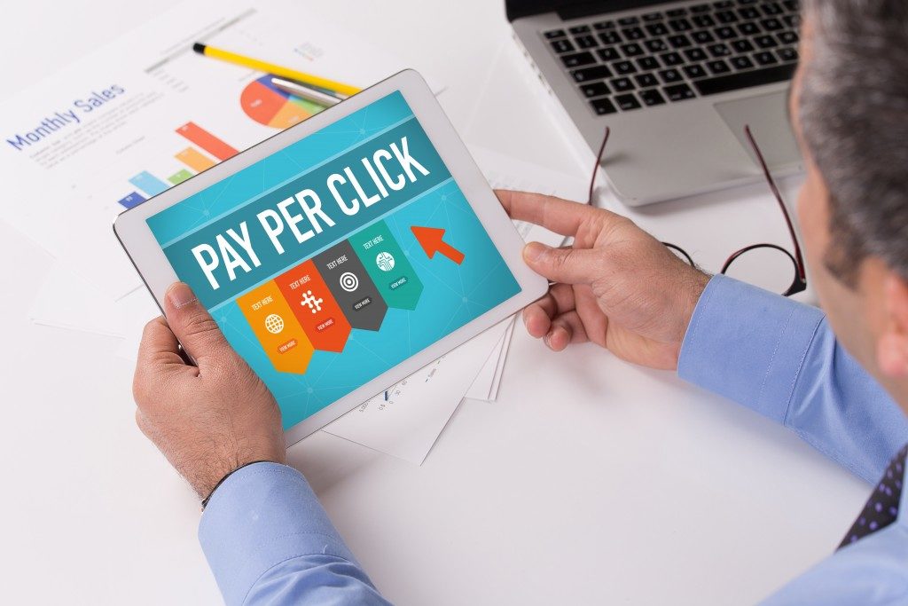 Man working on tablet with PAY PER CLICK on a screen
